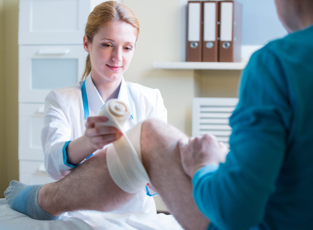 Female doctor is rewinding knee bandage to man.