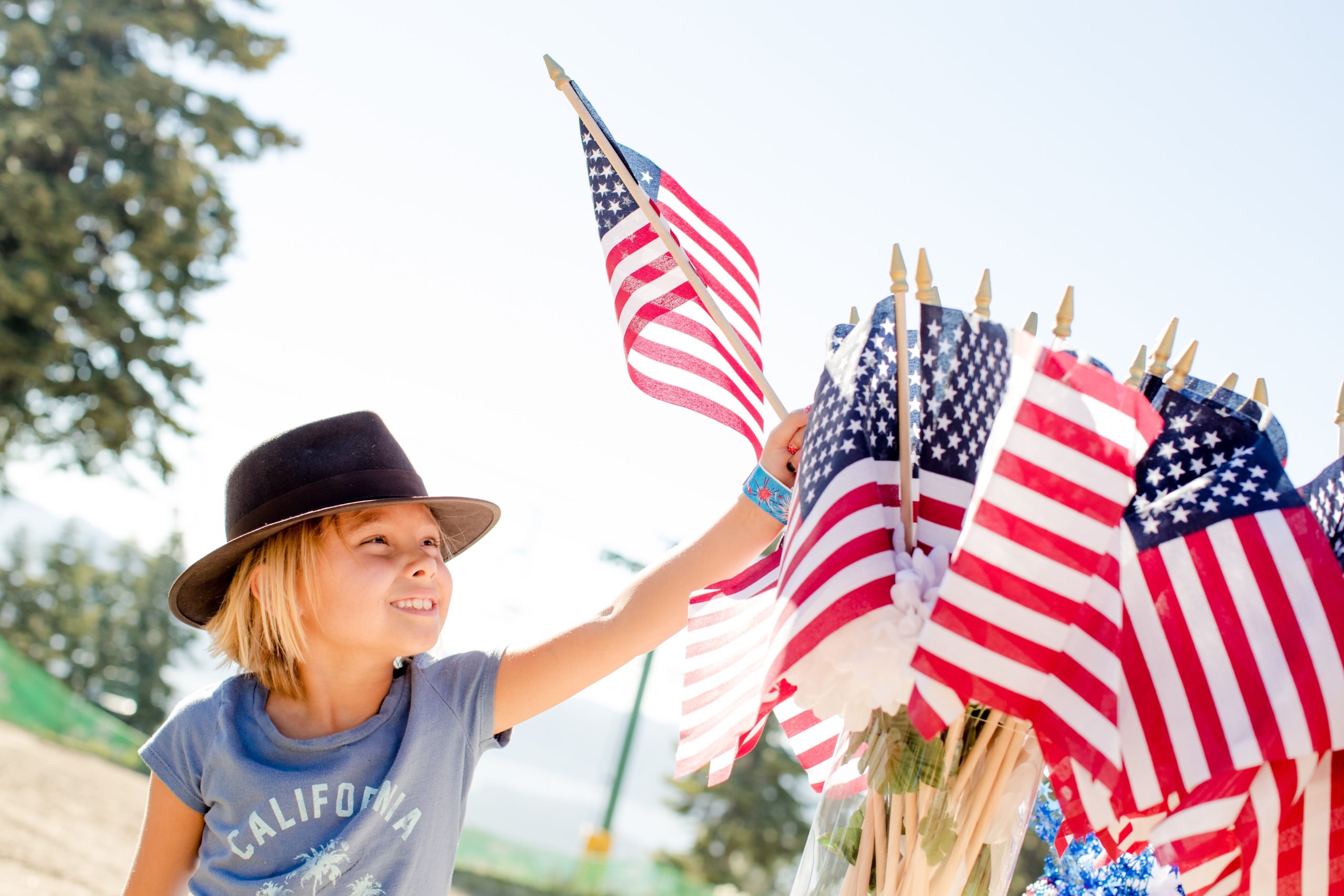 Young girl in a had waves an American flag at a independence day celebration.