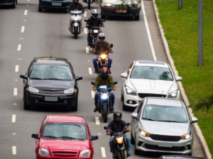 A line of motorcycles lane splitting between cars on the highway.