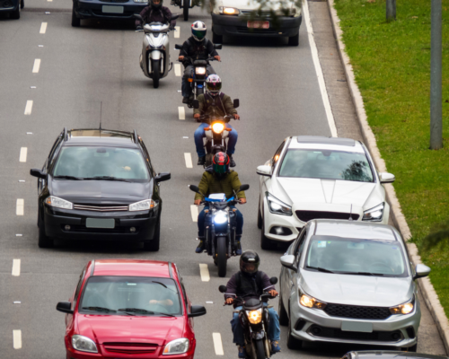 A line of motorcycles lane splitting between cars on the highway.