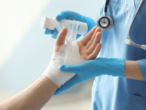 A gloved medical professional wraps a patients hand with gauze.
