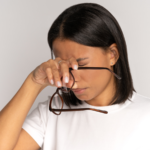 A woman rubbing her eyes holding her glasses.